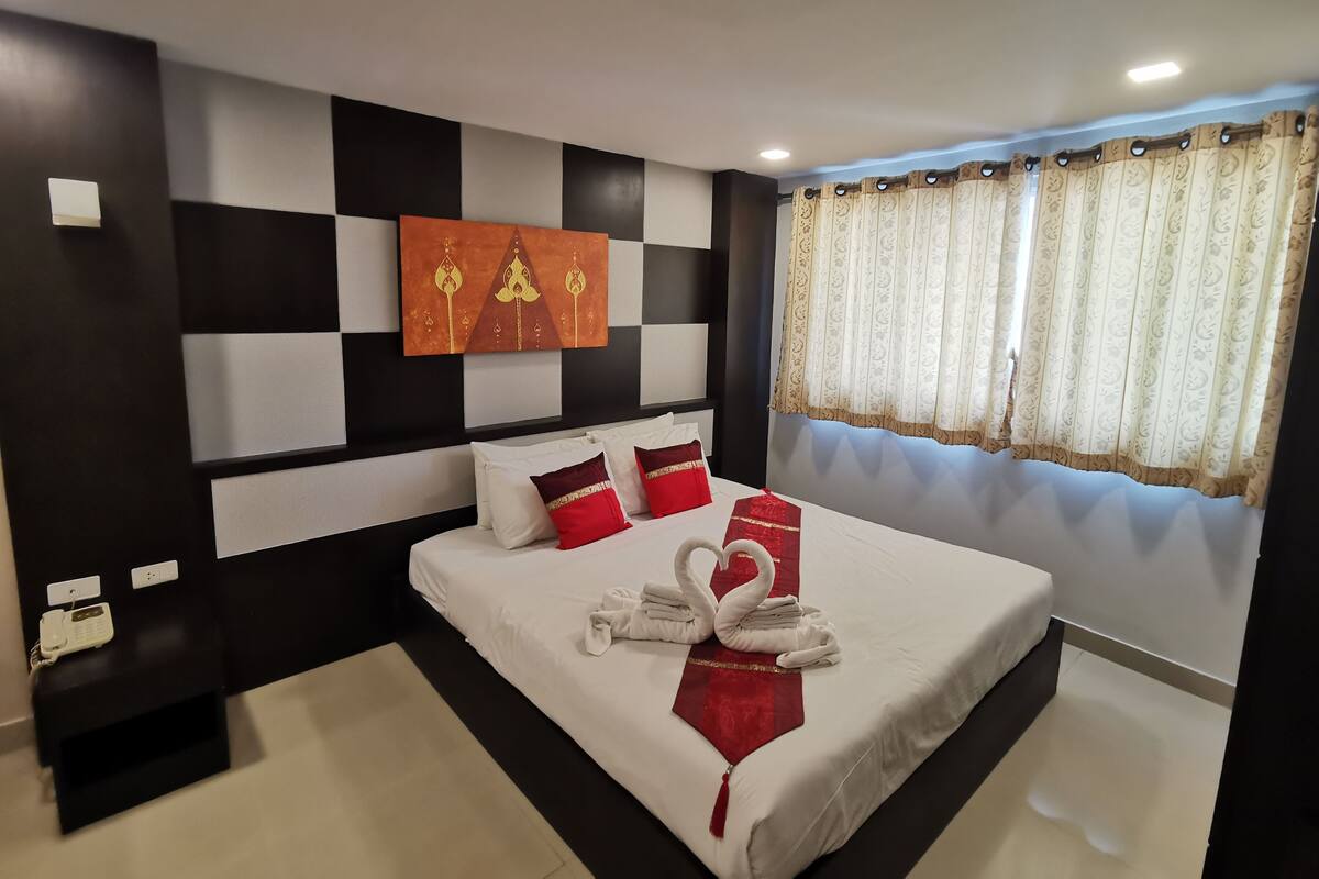 A modern hotel room with a large bed, black and white wall paneling, a decorative wall art piece, and a window with patterned curtains.