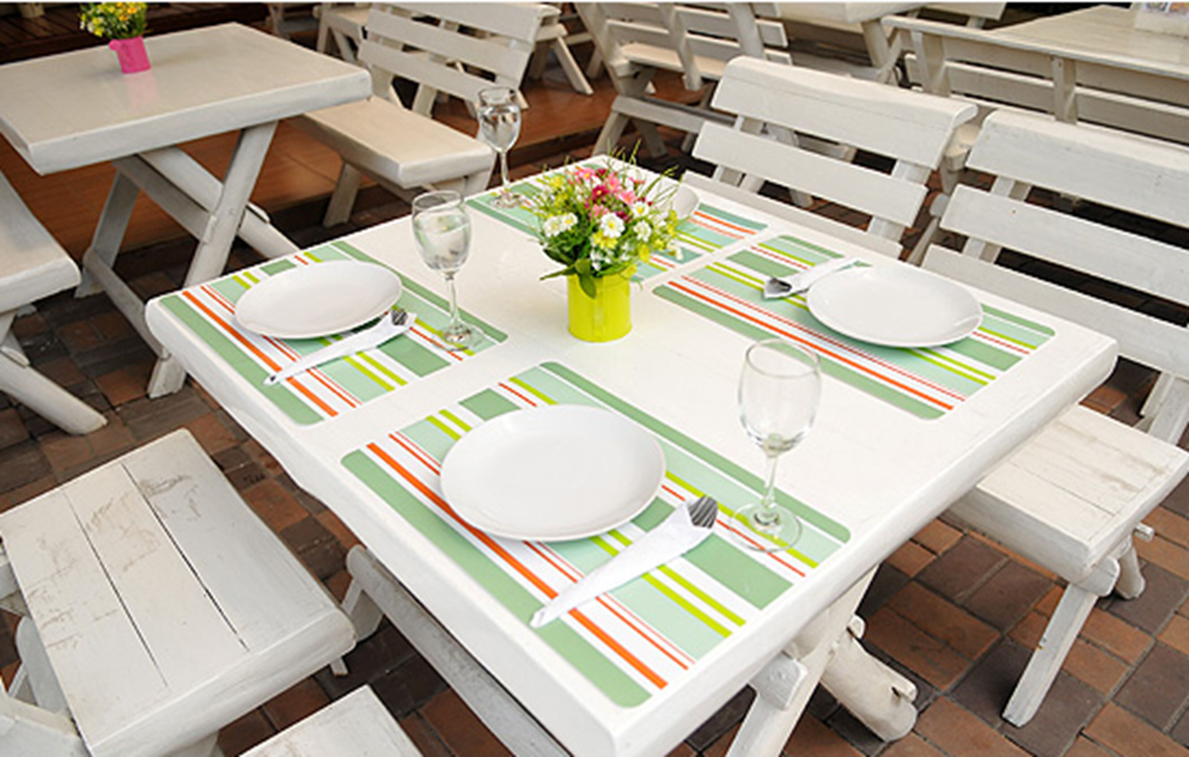 A dining table set with white plates, cutlery, and a glass of water, with a green and orange striped table runner.