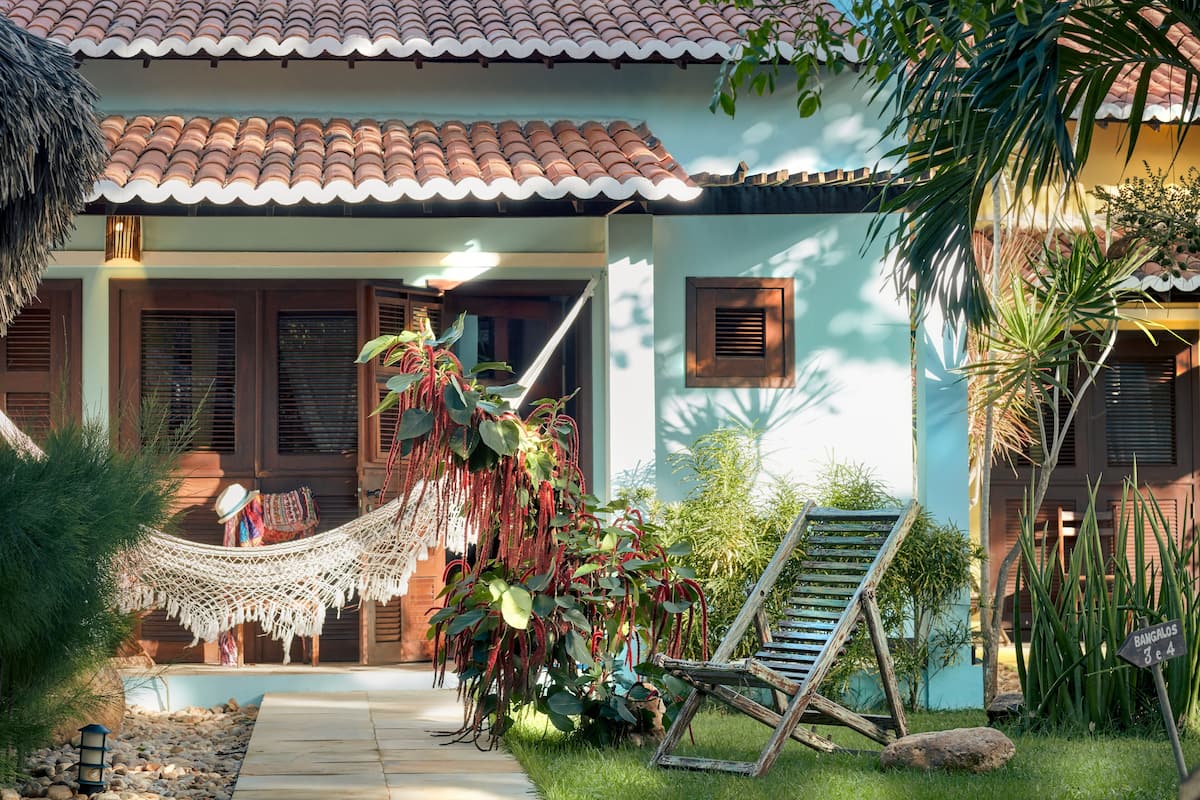 Uma casa com telhado de telhas, uma rede e uma cadeira no jardim.