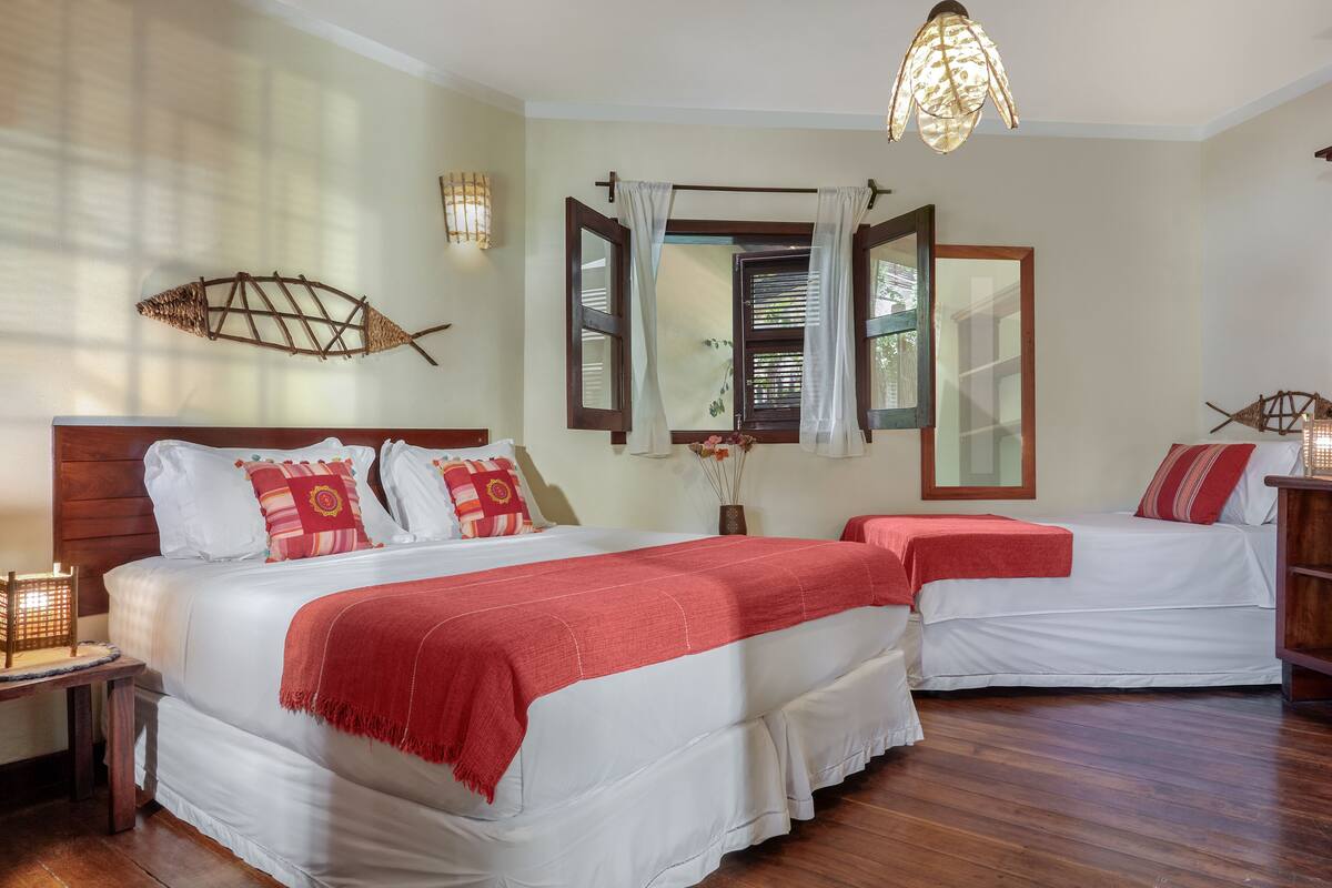 Quarto de hotel com duas camas, piso de madeira, uma grande decoração de peixe na parede e um candeeiro pendente.