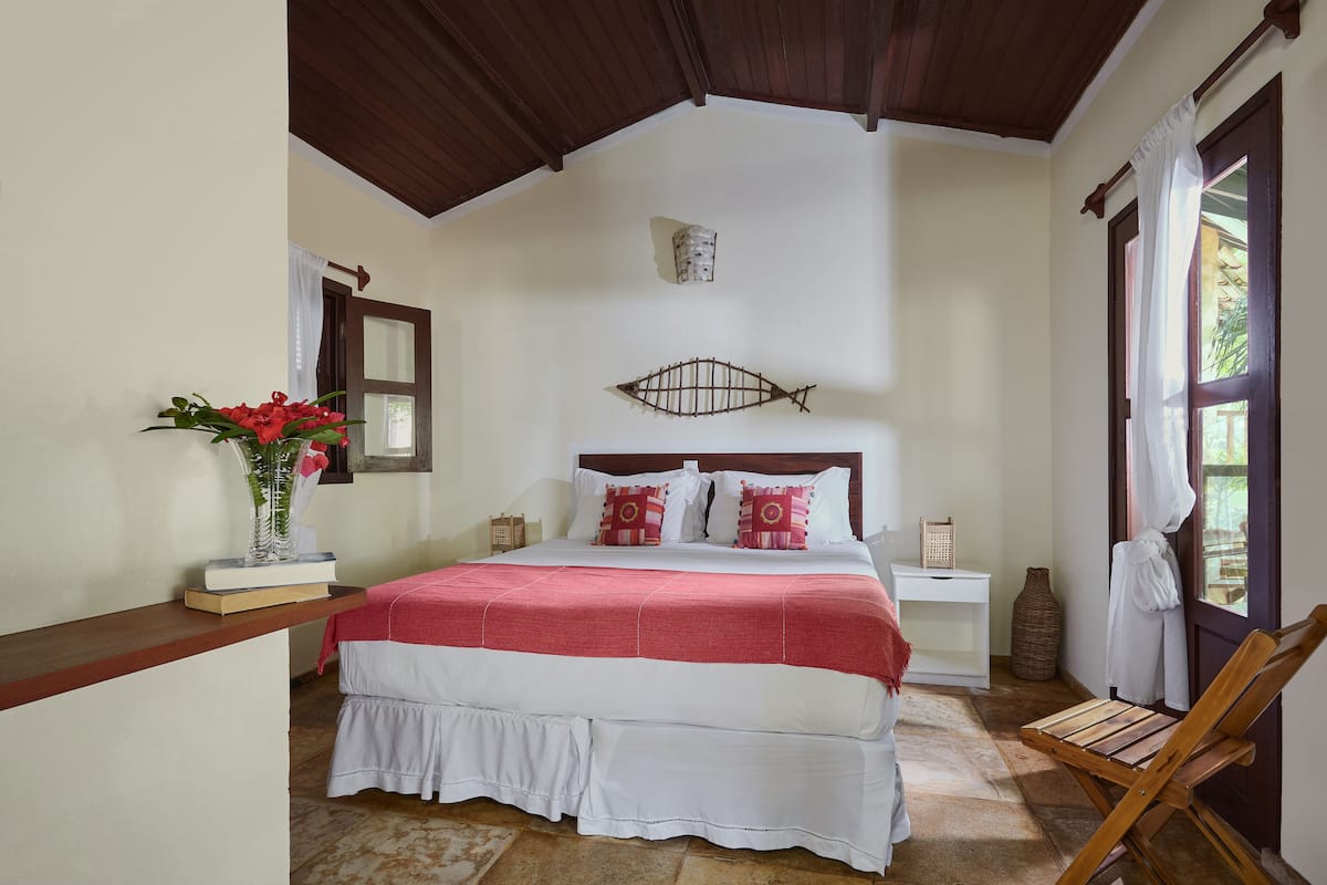 Quarto com cama, mesa de cabeceira, cadeira de madeira, vaso com flores e decoração de parede em formato de peixe.
