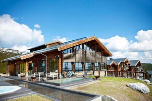 Un moderno alojamiento con fachada de vidrio amplia, piscina exterior y terraza de madera.