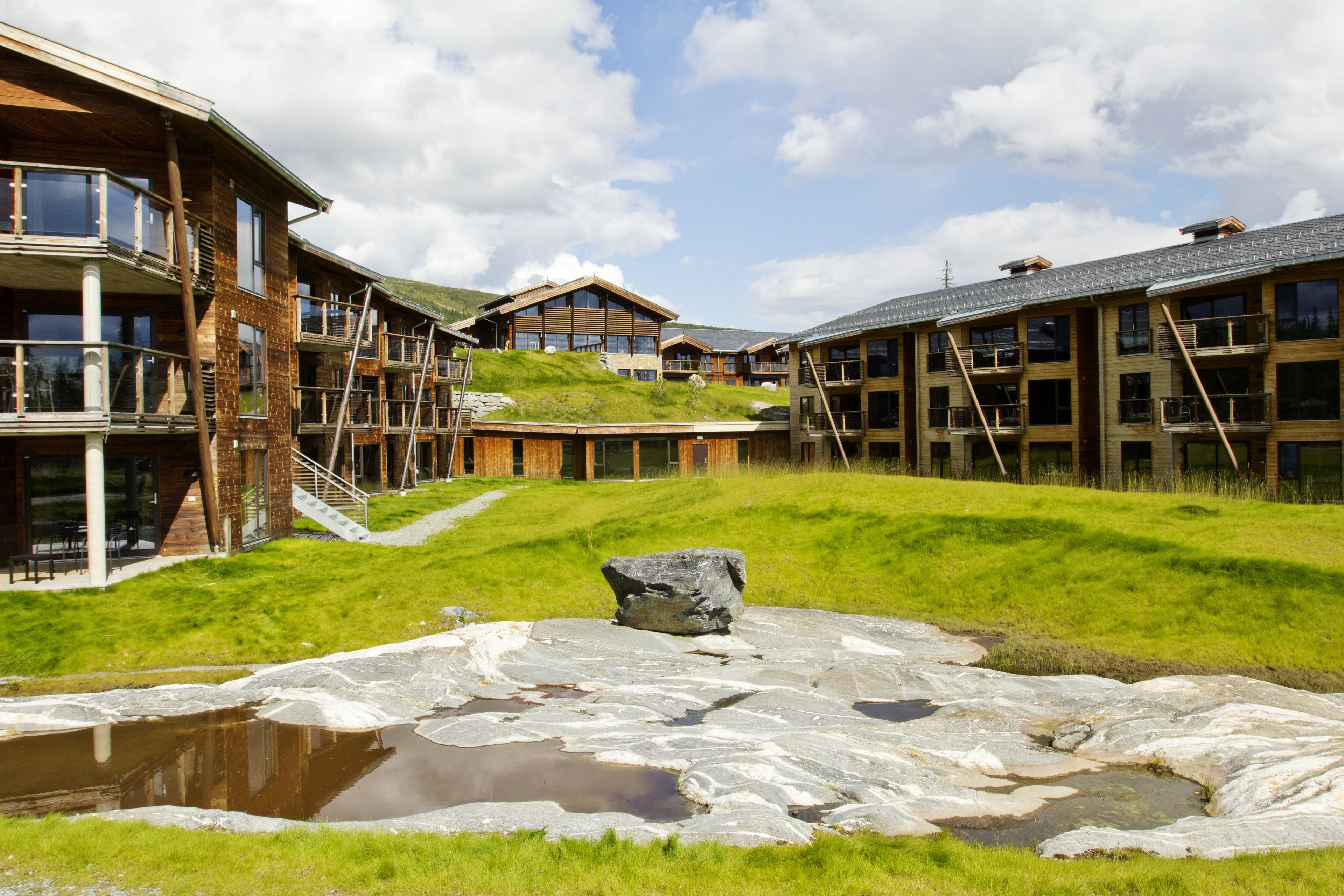 A modern building with multiple balconies, a grassy area, and a small pond.