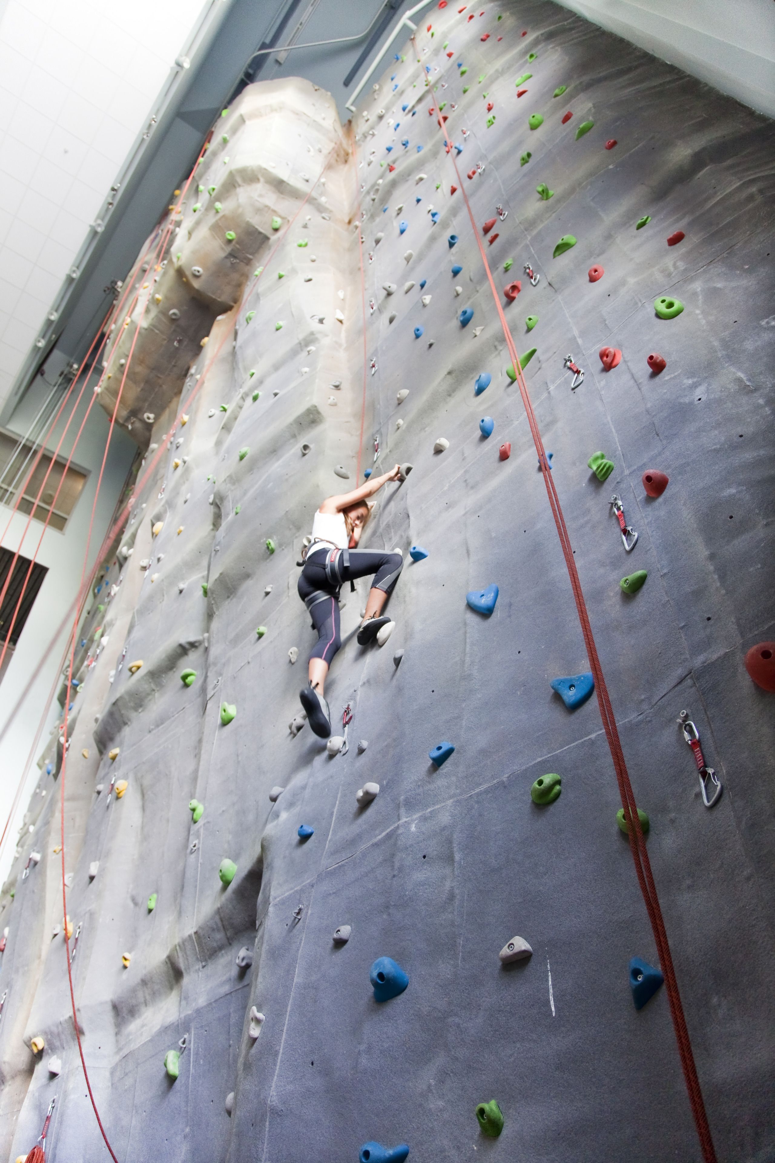 A person climbing a large indoor rock wall with various colored holds.