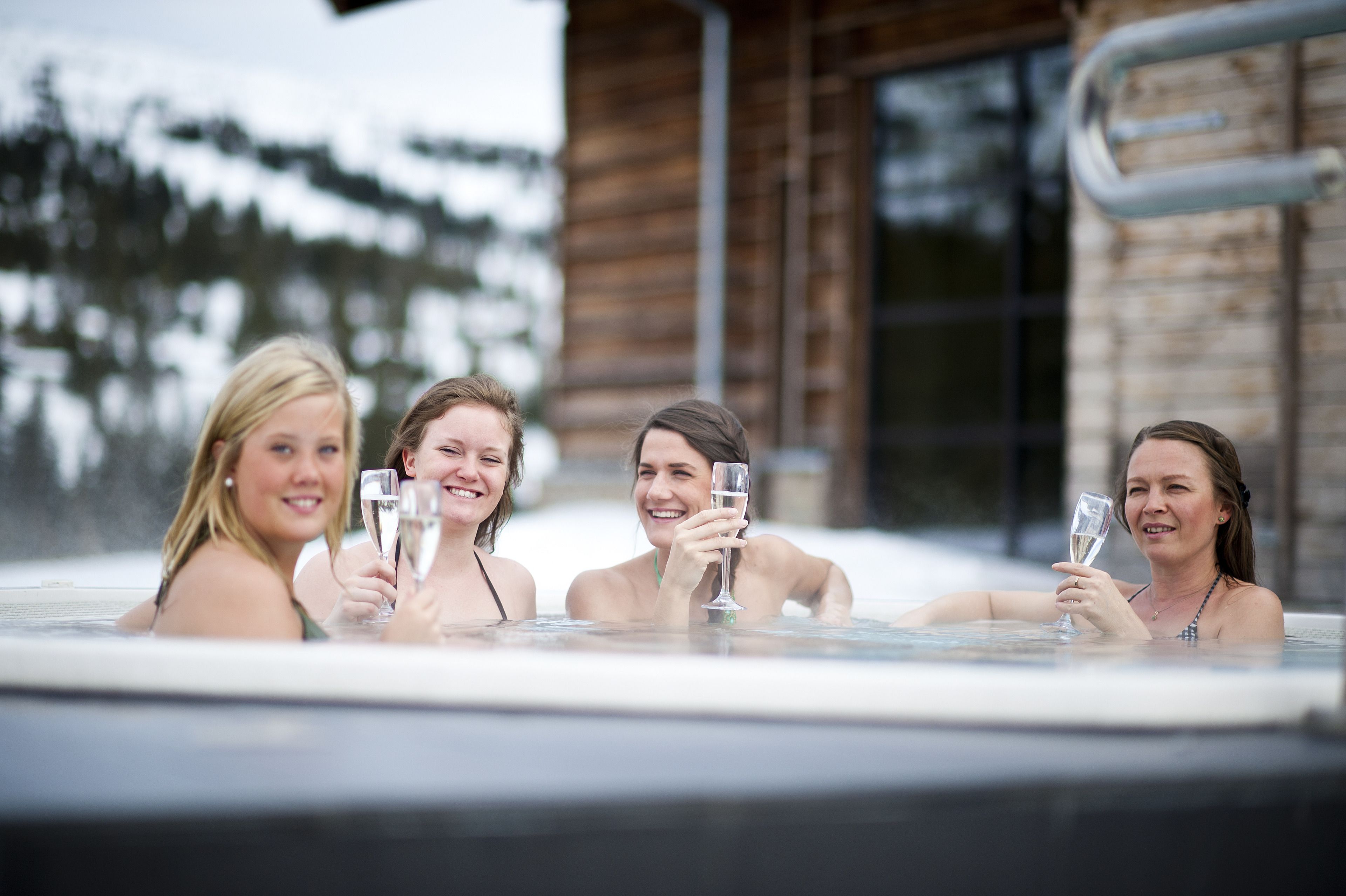 Four people in a hot tub with a wooden cabin in the background.