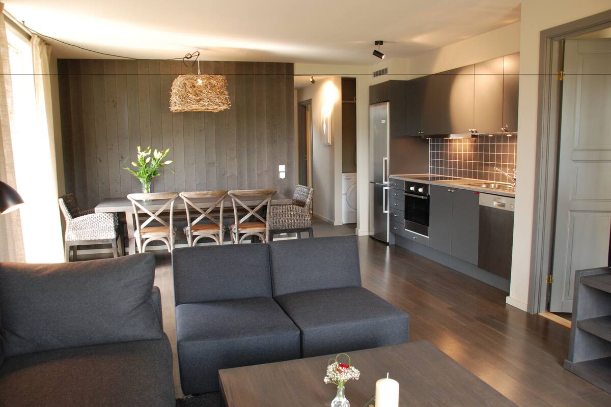 A modern living room with a sofa, a dining table with chairs, and a kitchen area with cabinets and appliances.