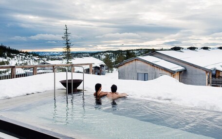 A couple in a hot tub with a snowy landscape and buildings in the background.