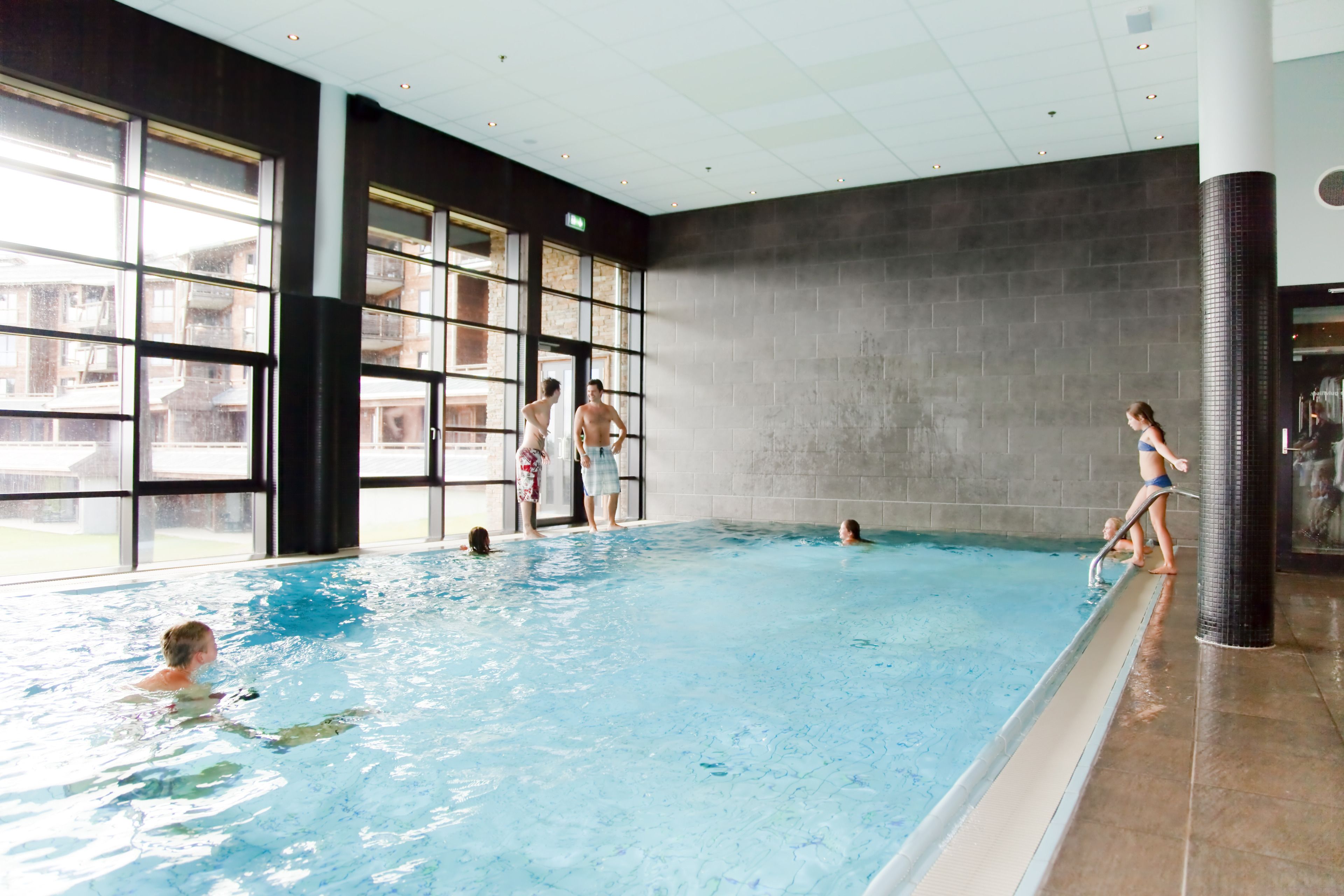 An indoor swimming pool with clear glass walls, a tiled floor, and a view of buildings outside.