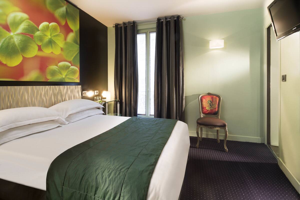 A hotel room with a large bed, a chair, a TV, and a window with curtains.