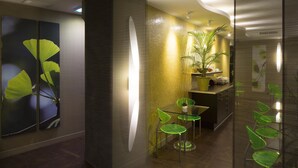 A modern interior with a glass partition, a green plant, and a small dining area with a table and chairs. - Le Fabe Hotel (Paris)