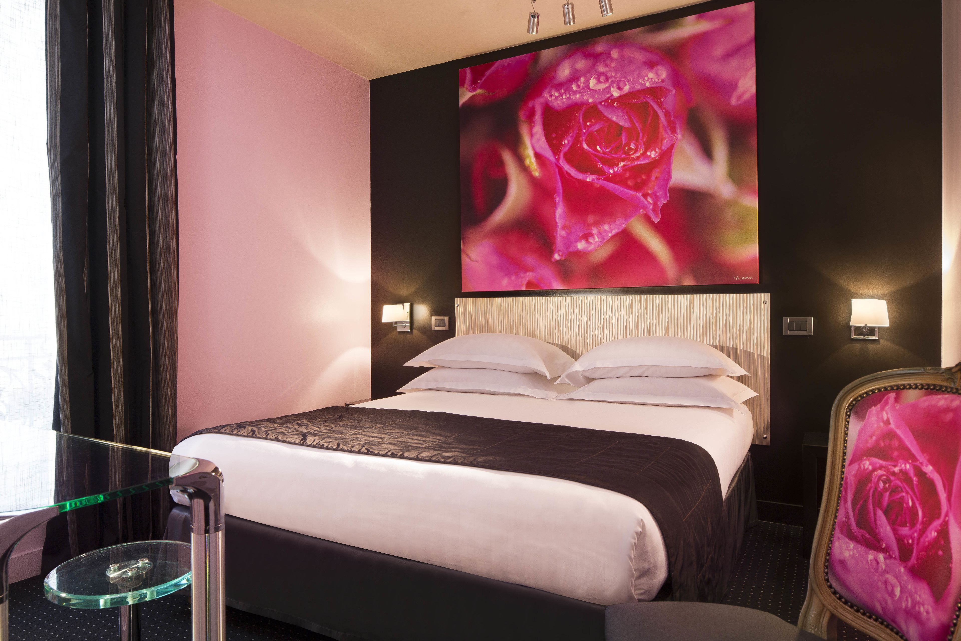 Quarto de hotel com uma cama grande, uma mesinha de vidro, uma cadeira com desenho de rosa e uma obra de arte pendurada na parede retratando uma rosa.