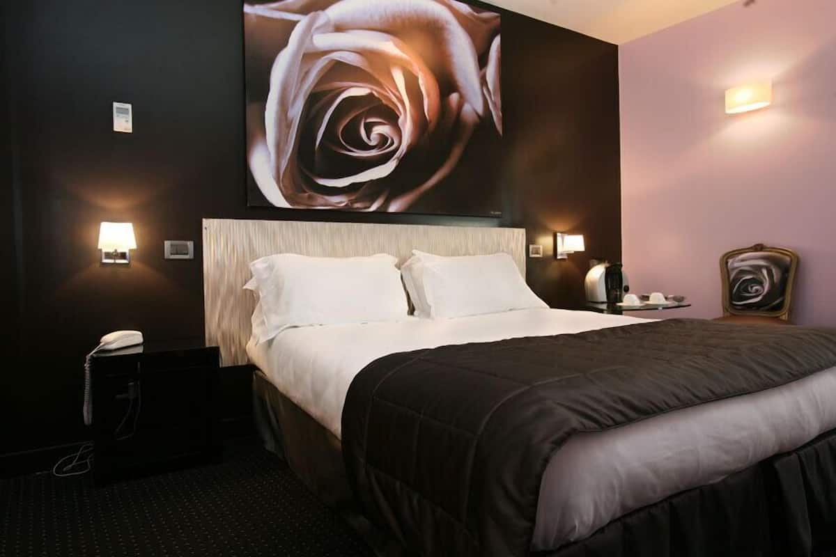 A hotel room with a large bed, two bedside lamps, a wall-mounted TV, and a large floral artwork above the bed.