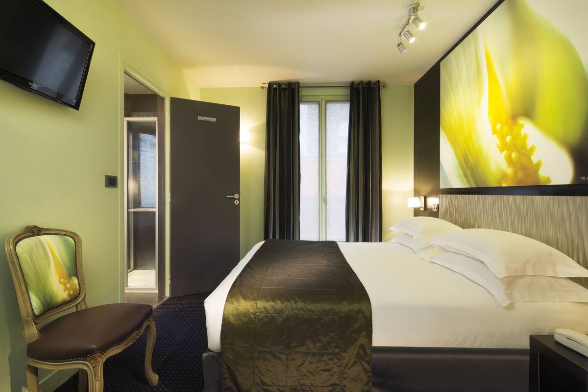 A hotel room with a bed, a chair, a TV, and a large window with curtains.