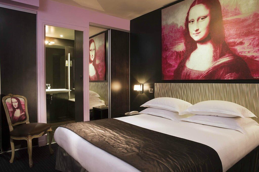 A hotel room with a large bed, a chair, a mirror, and a painting of the Mona Lisa on the wall.