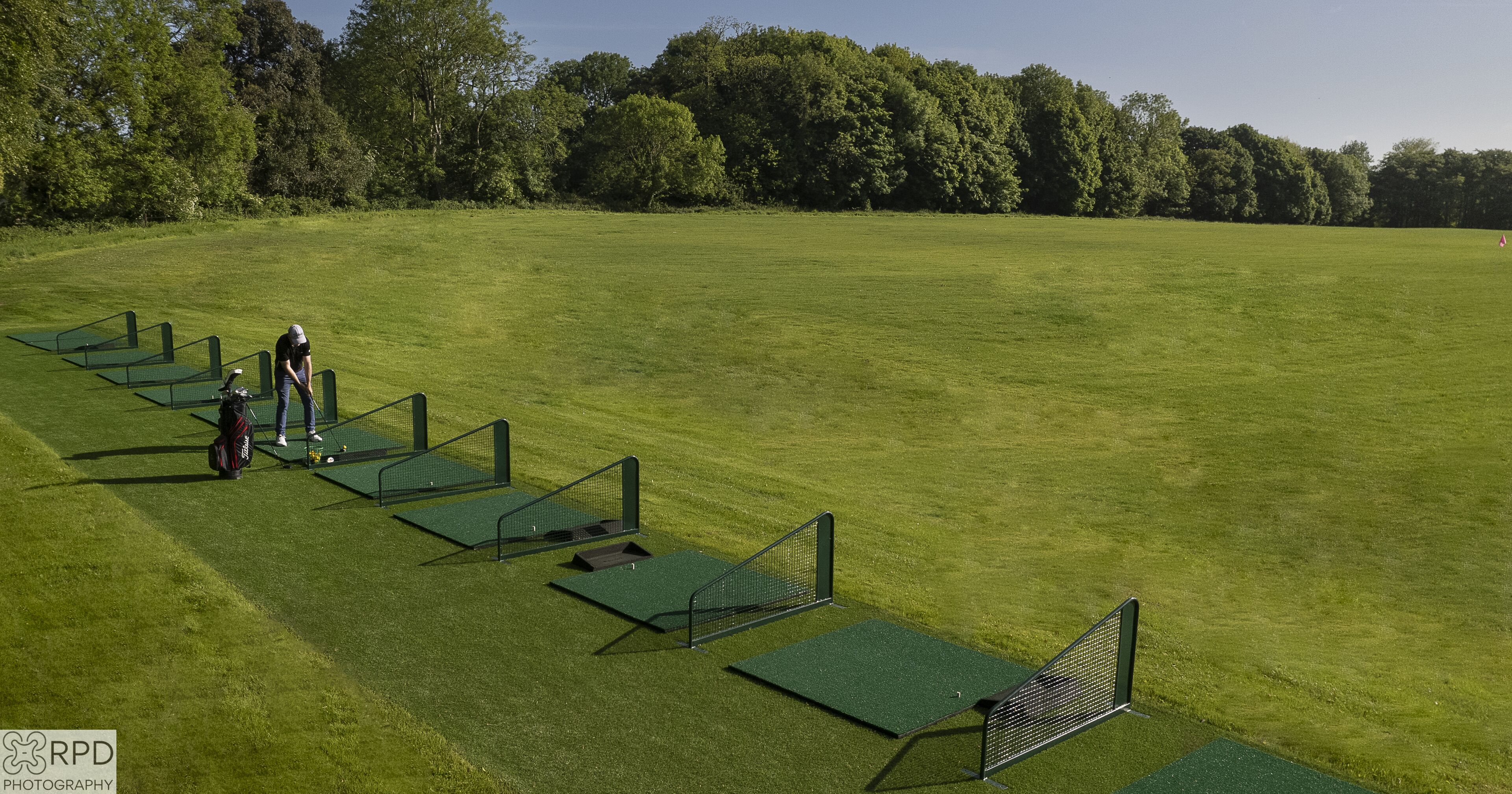 Ein Golfplatz mit mehreren Übungsgrüns und einer Person, die sich zum Putten vorbereitet.