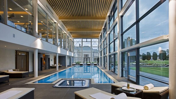 Una piscina interior moderna con zonas de descanso y grandes ventanales que ofrecen vistas del paisaje circundante.