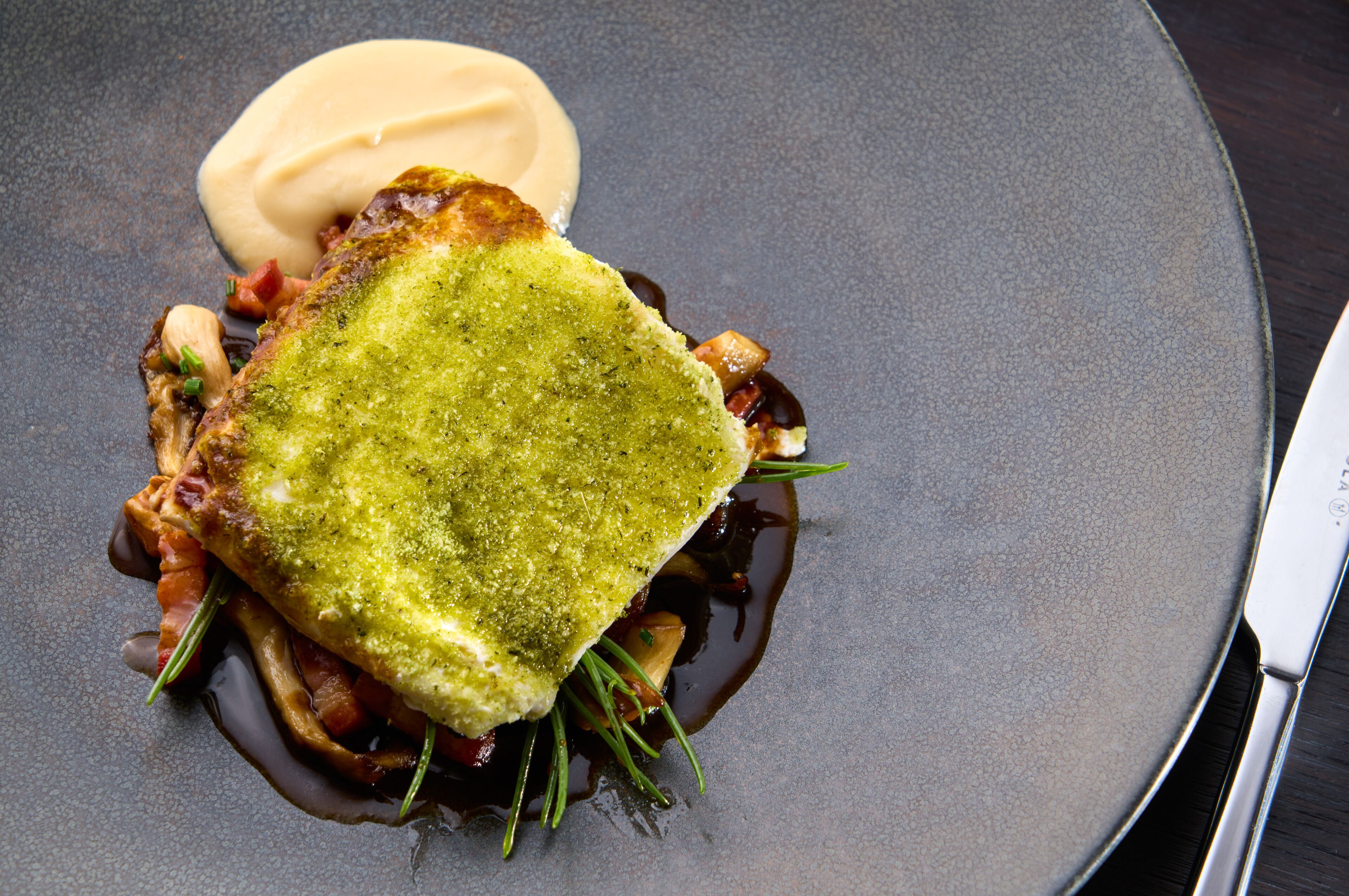 A dish with a green topping, sauce, and herbs on a plate.