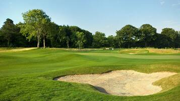 A golf course with a sand bunker and trees in the background.