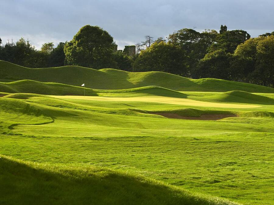 A golf course with undulating terrain and a flag marking the hole.