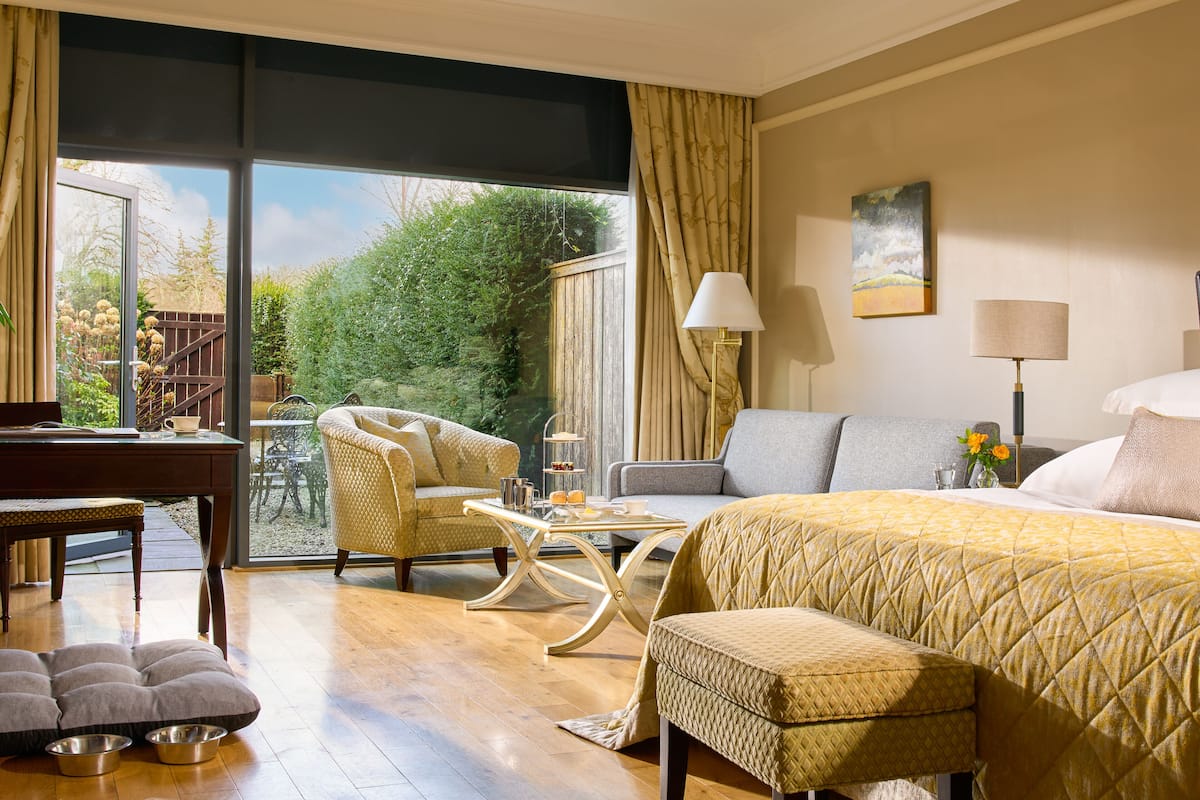 A hotel room with a large bed, a sofa, a dining table, and a piano.