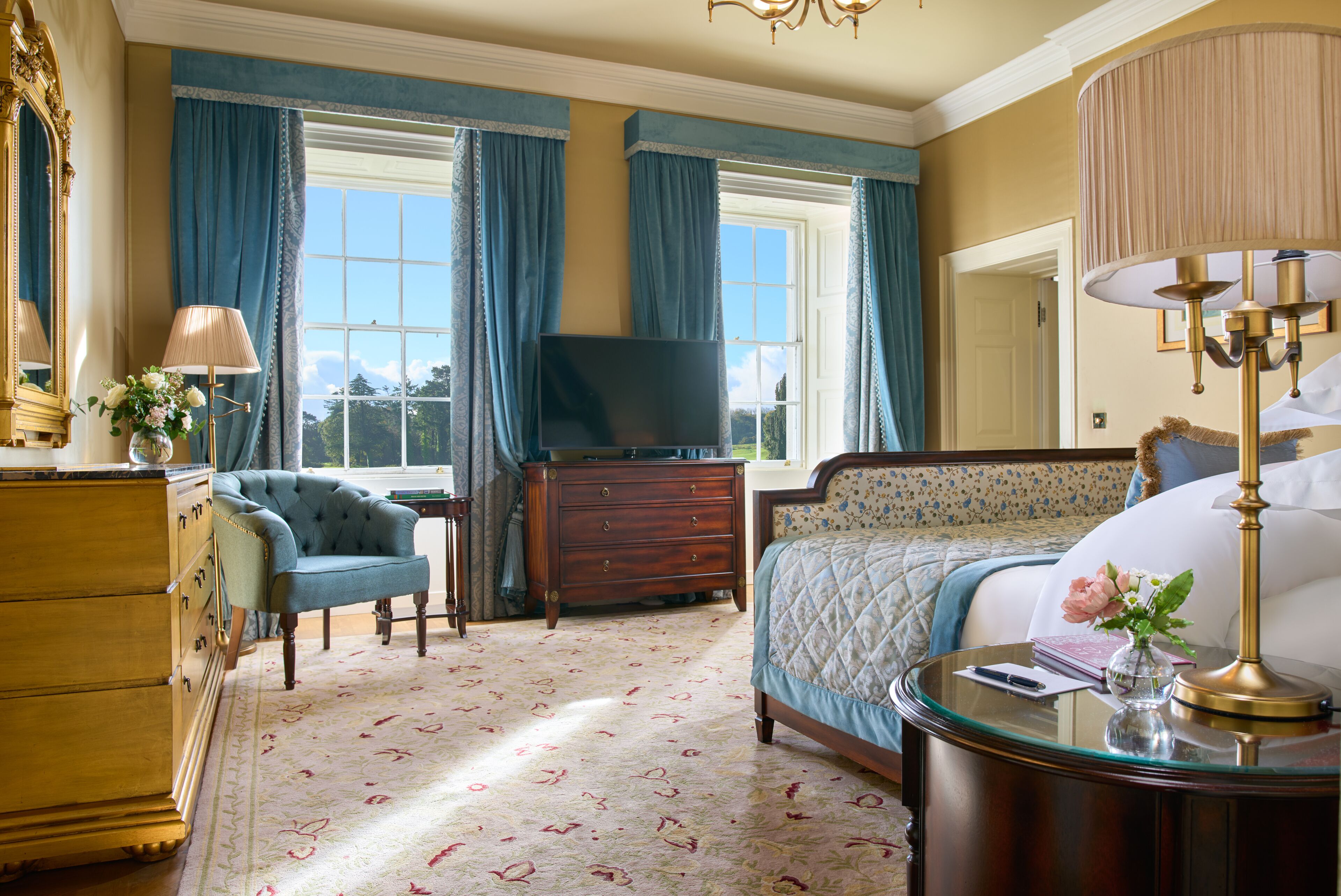 A bedroom with a bed, dresser, vanity, and a television.