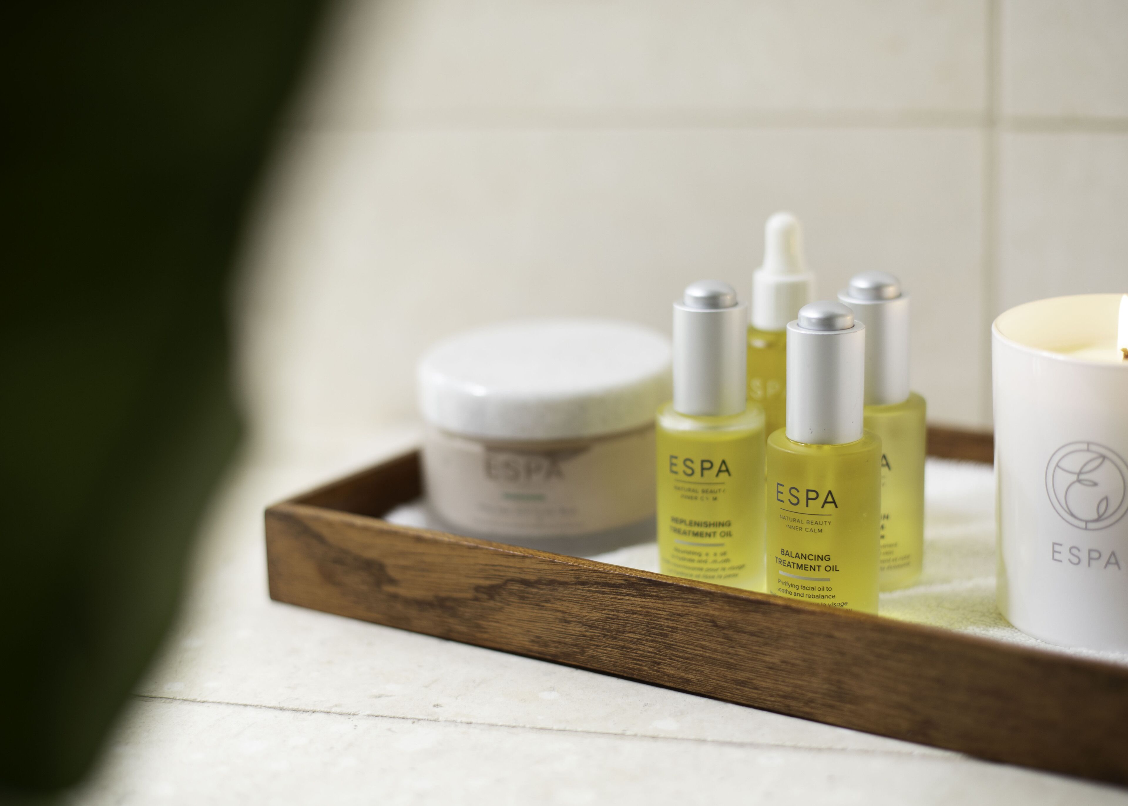 A wooden tray with skincare products, including a jar and bottles labeled ESPA, on a tiled surface.