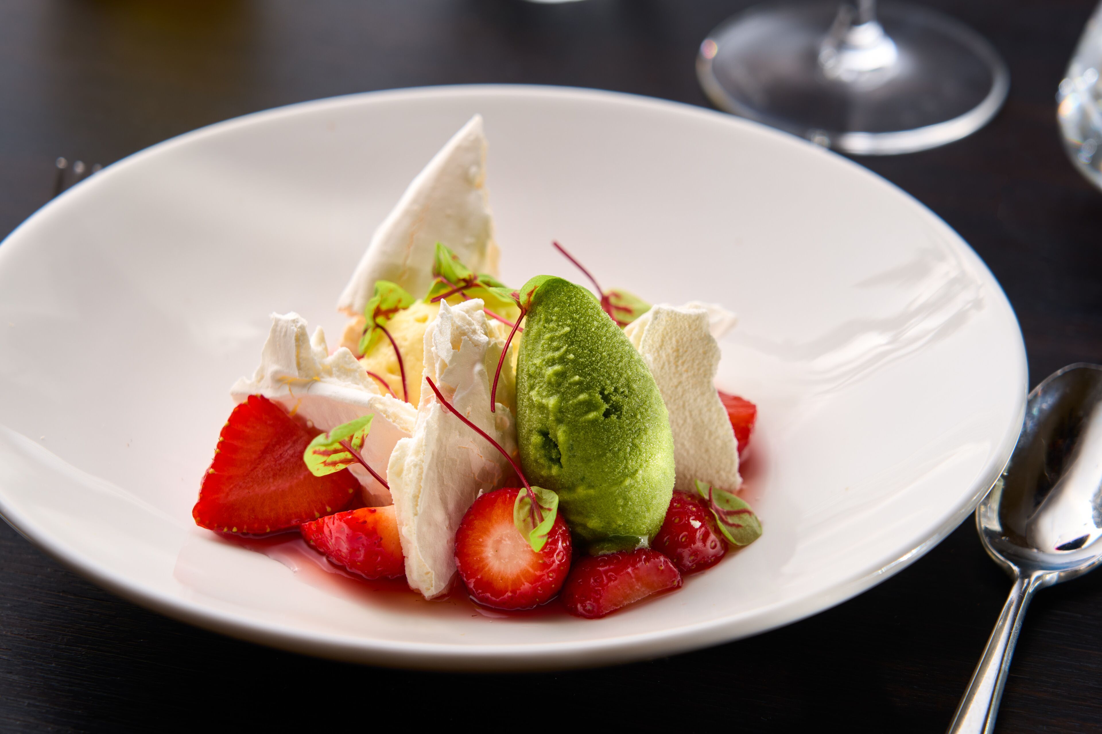 Un plato blanco con un postre de fresas, una porción de helado verde y un trozo de pastel blanco.