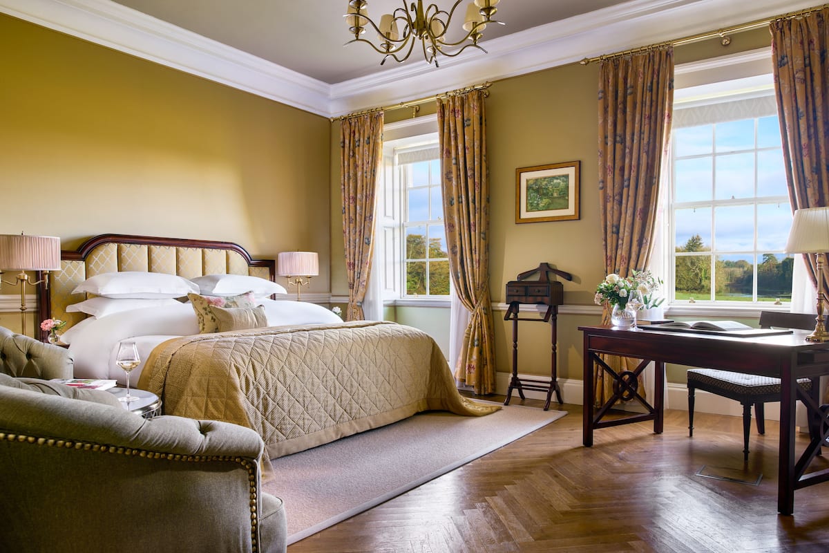 A well-appointed bedroom with a large bed, a desk, and a chair, featuring a view of the outdoors through a window.