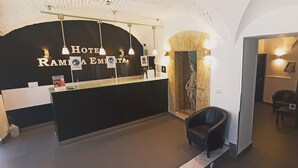 A hotel reception area with a black counter, a reception desk, and a seating area with a chair. - Hotel Rambla Emérita (Merida)