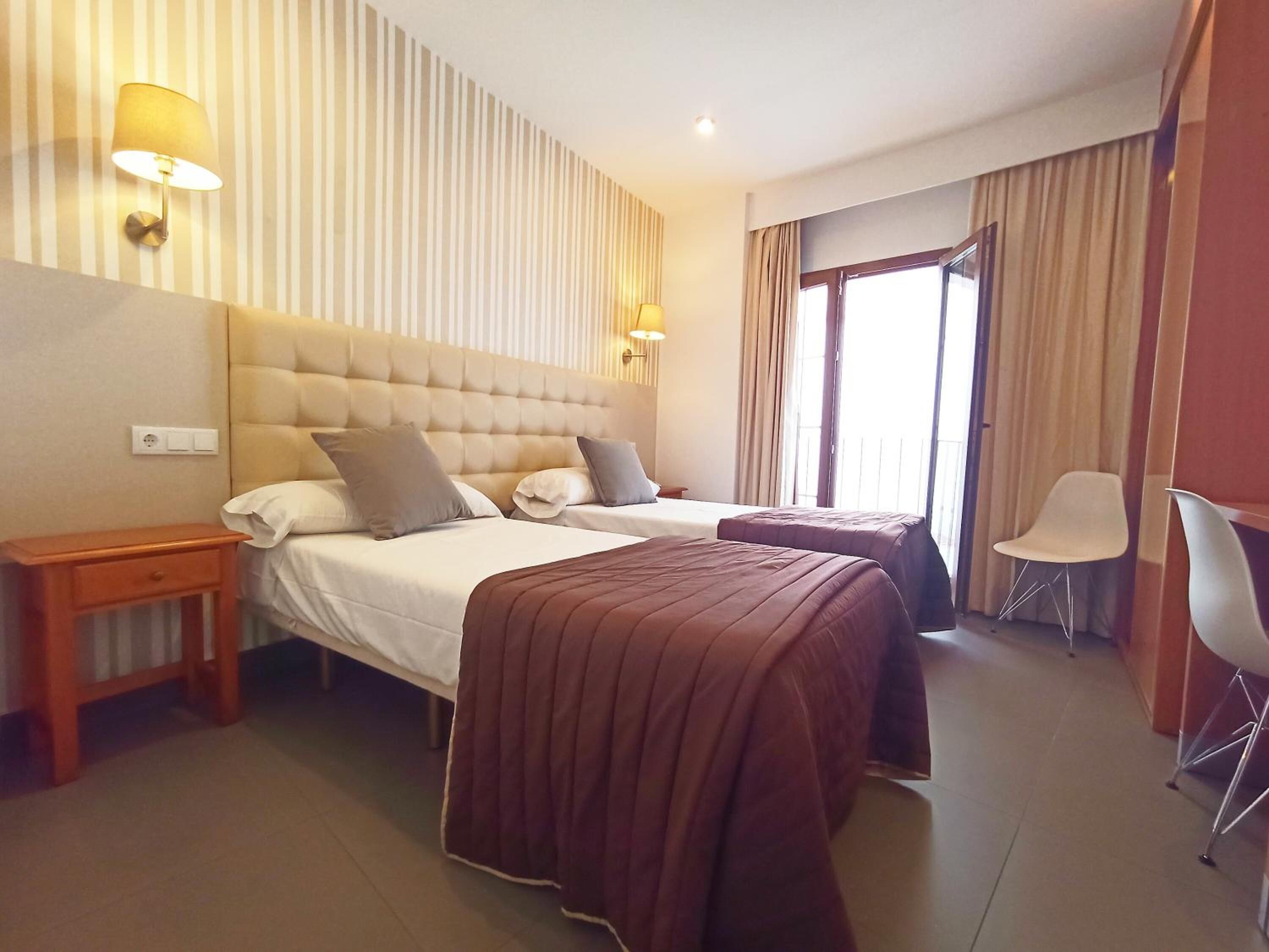 Habitación de hotel con una cama grande, dos mesitas de noche, una silla y una ventana con cortinas.