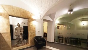 A lobby with a marble statue, a black leather chair, and a glass wall with the hotel name. - Hotel Rambla Emérita (Merida)