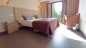 A bedroom with a bed, bedside lamps, a nightstand, a window with curtains, and a balcony view. - Hotel Rambla Emérita (Merida)