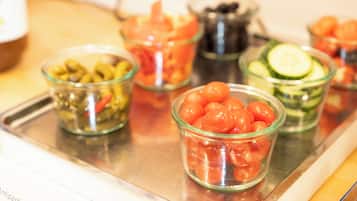 Un plateau contenant divers aliments, notamment des olives, des tomates, des concombres et des olives dans un récipient en verre.