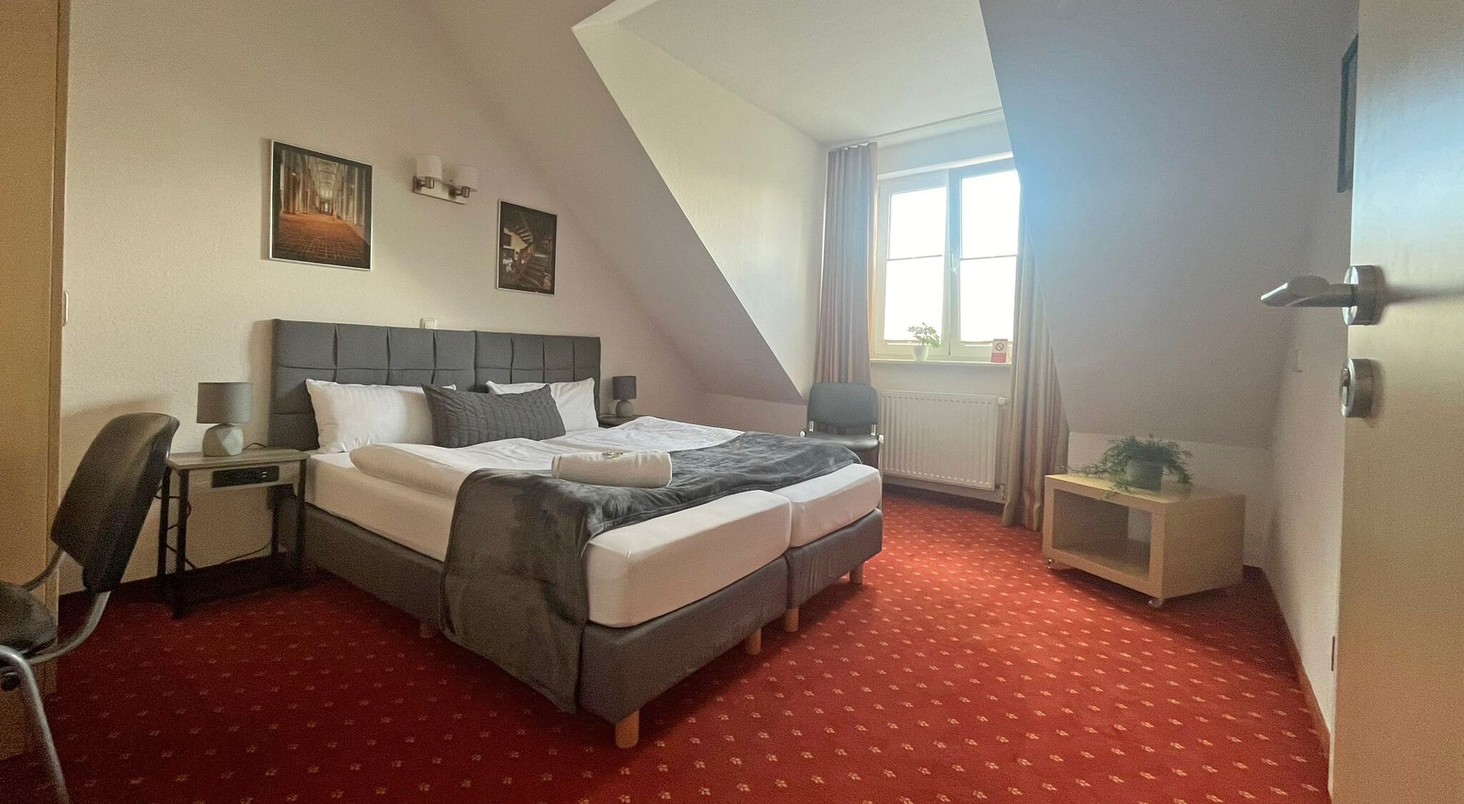 A hotel room with a bed, a desk, a chair, a small table, and a window with curtains.