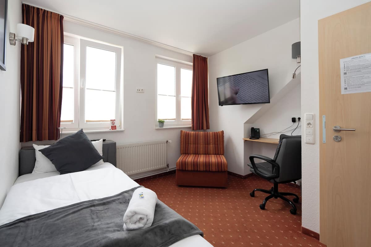 A hotel room with a bed, a desk, a chair, a TV, and a window.