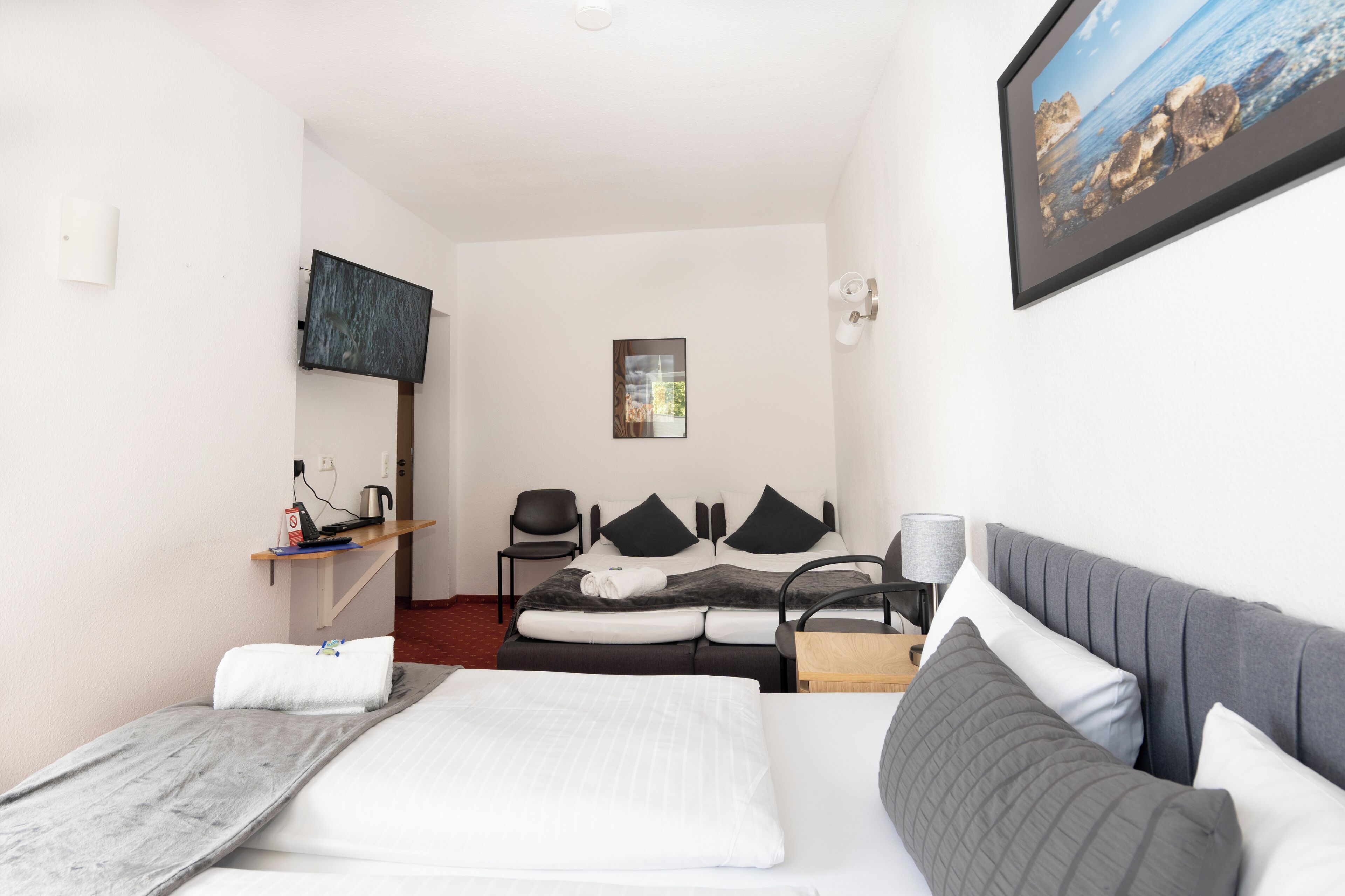 A hotel room with a bed, a desk with a chair, a TV, and a framed picture on the wall.