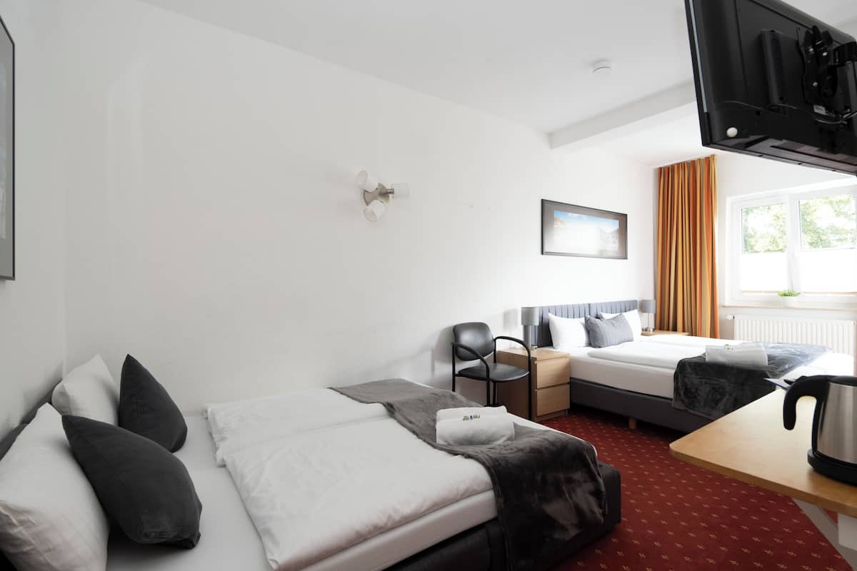 A hotel room with a bed, a desk, a chair, a TV, and a window with curtains.