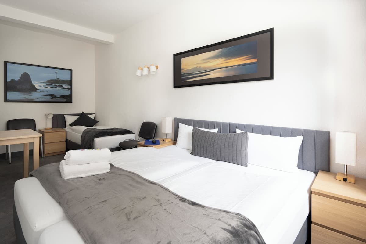 A hotel room with a large bed, a desk, a chair, a nightstand, and two wall-mounted lamps.