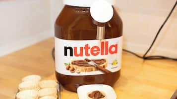 Ein Nutella-Glas mit einem Löffel und eine kleine Schale Nutella auf einer Holzoberfläche.