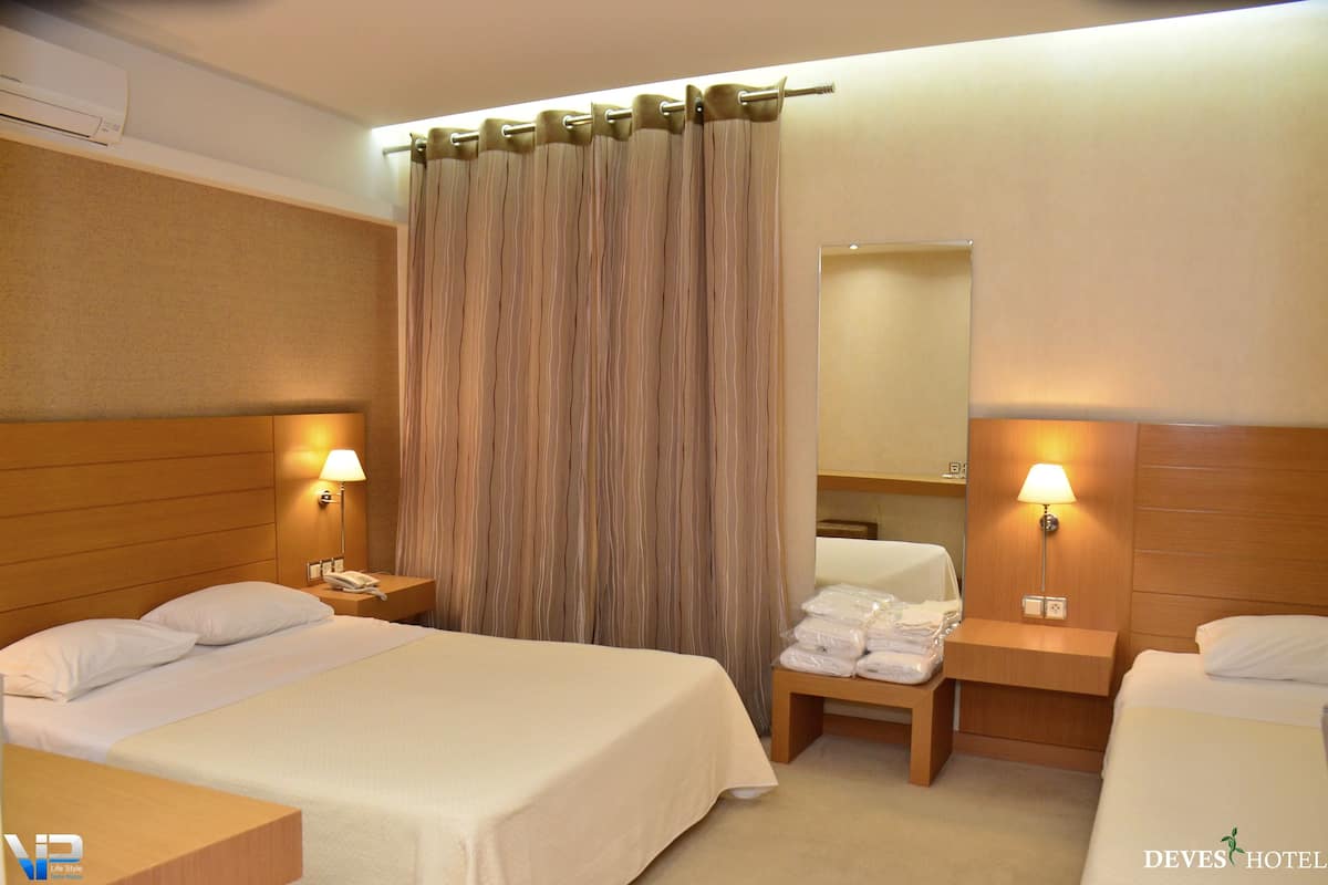 A hotel room with two beds, a wooden headboard, a mirror, a bedside table with a lamp, and a curtain.