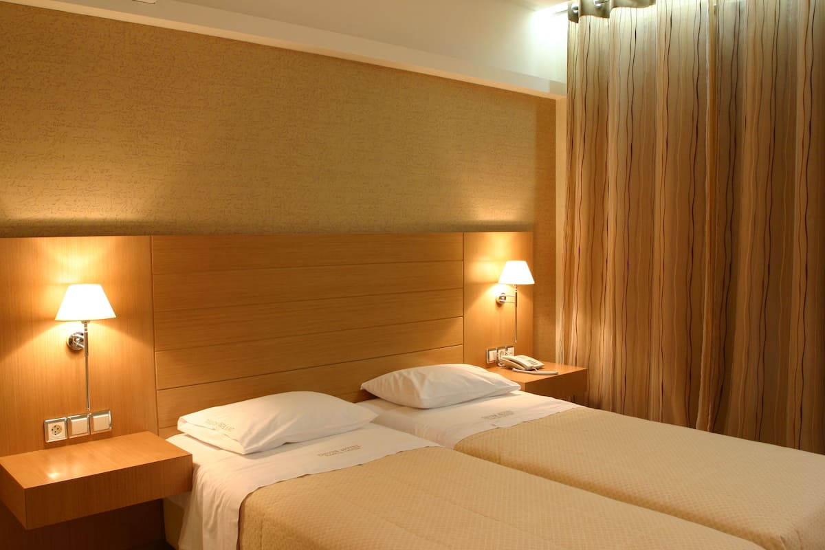 A hotel room with two beds, wooden headboard, bedside lamps, and a telephone on the nightstand.