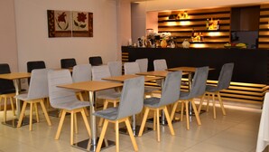 Ein modernes Café mit Holztischen und grauen Stühlen, einer Theke mit Getränken und Snacks sowie Bildern an der Wand.