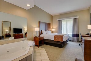A hotel room with a large bed, a separate bathroom with a bathtub, a television, and a desk with a lamp.