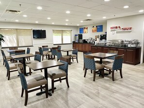 A restaurant with multiple tables and chairs, a kitchen area, and a motivational sign on the wall.