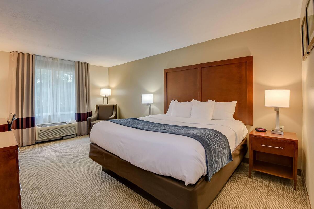 A hotel room with a large bed, two bedside tables with lamps, a chair, and a window with curtains.