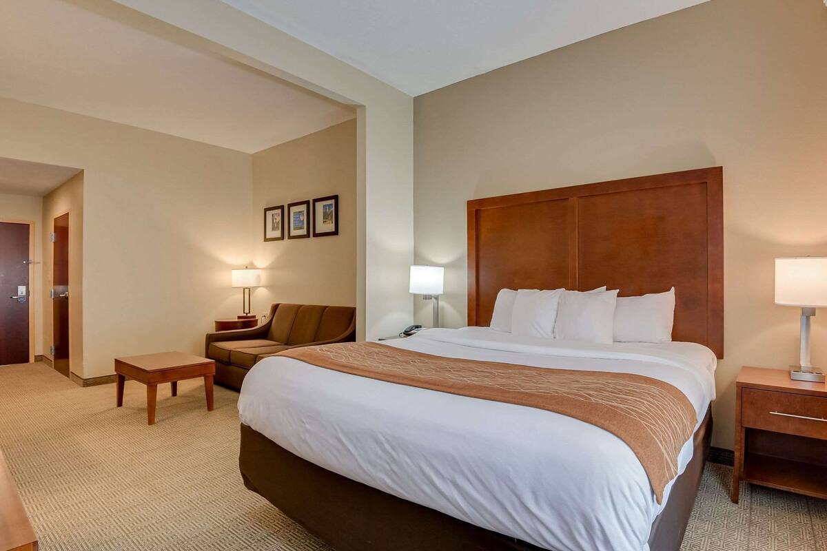 Quarto de hotel com uma cama grande, uma escrivaninha, uma cadeira e uma mesa de cabeceira.