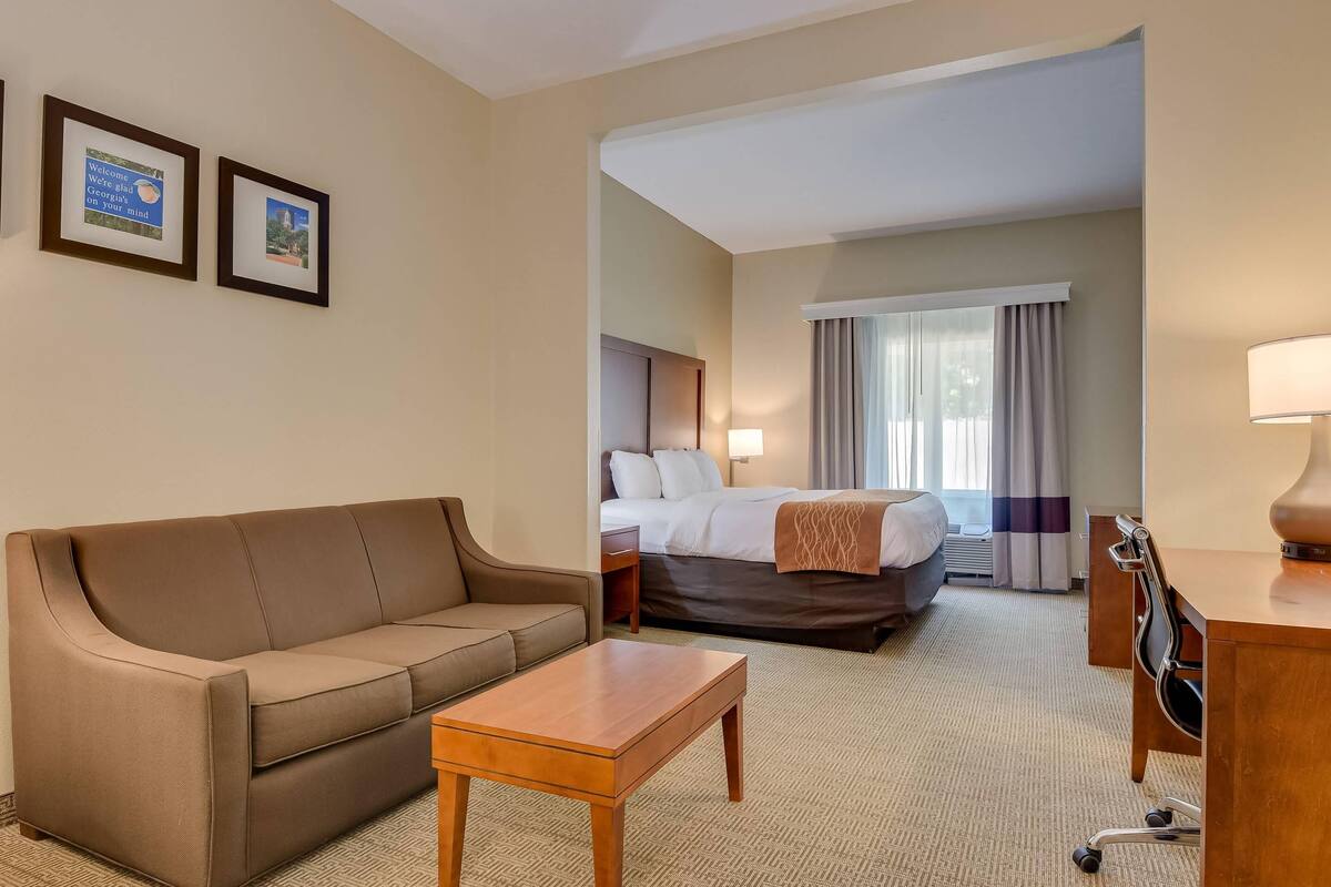 A hotel room with a sofa, a bed, a desk, and two framed pictures on the wall.