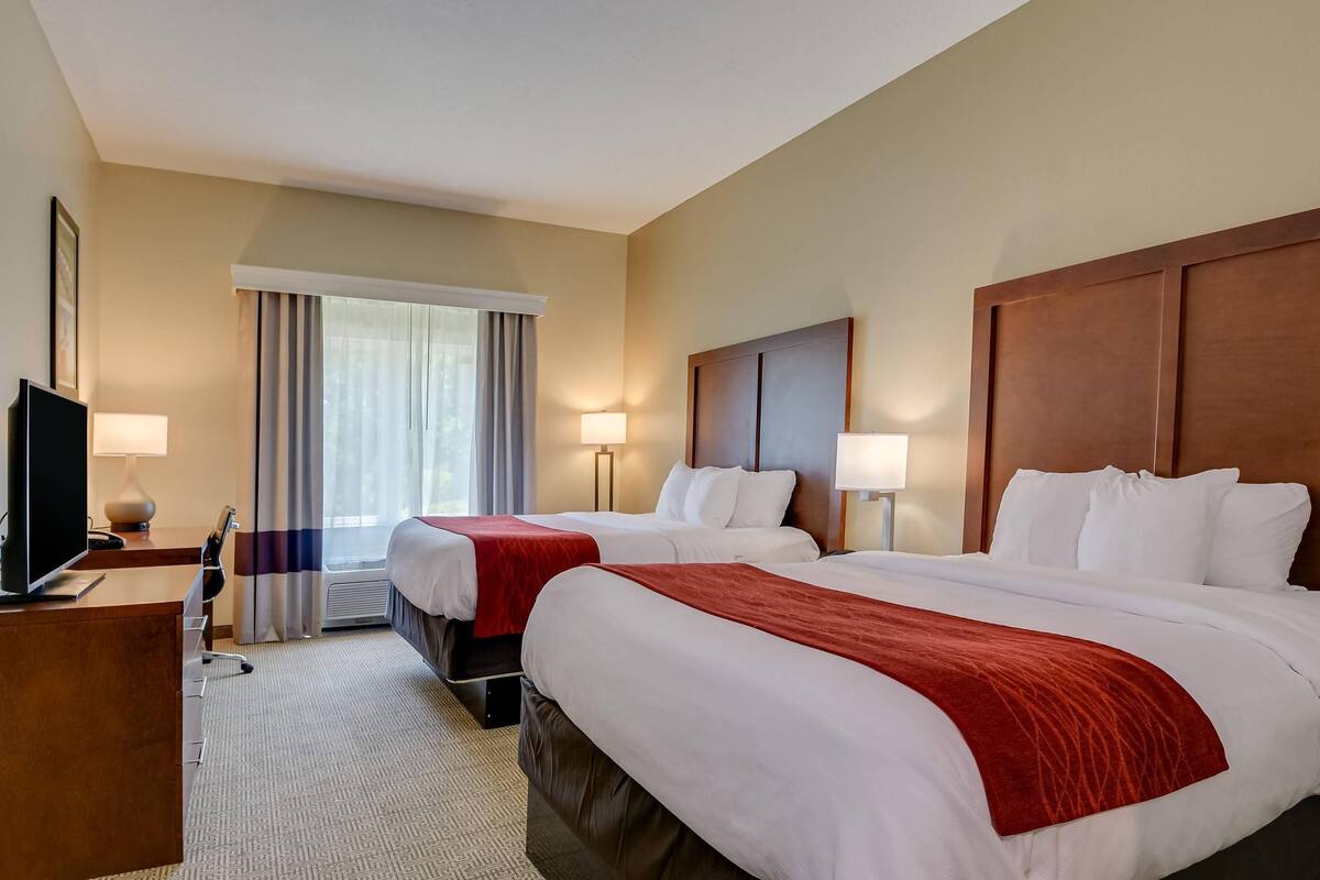 A hotel room with two beds, a desk, a TV, and a window with curtains.