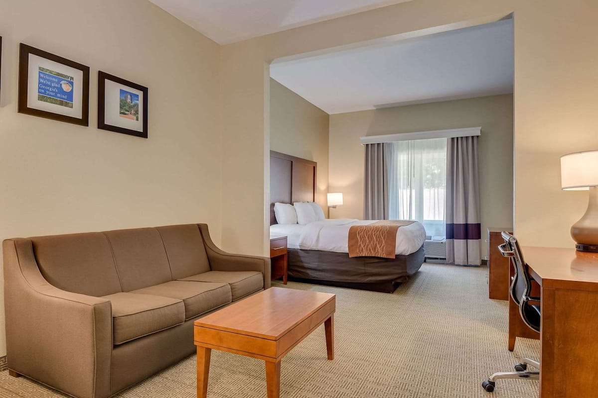 Quarto de hotel com sofá, uma cama de solteiro, escrivaninha com luminária e dois quadros de boas-vindas.