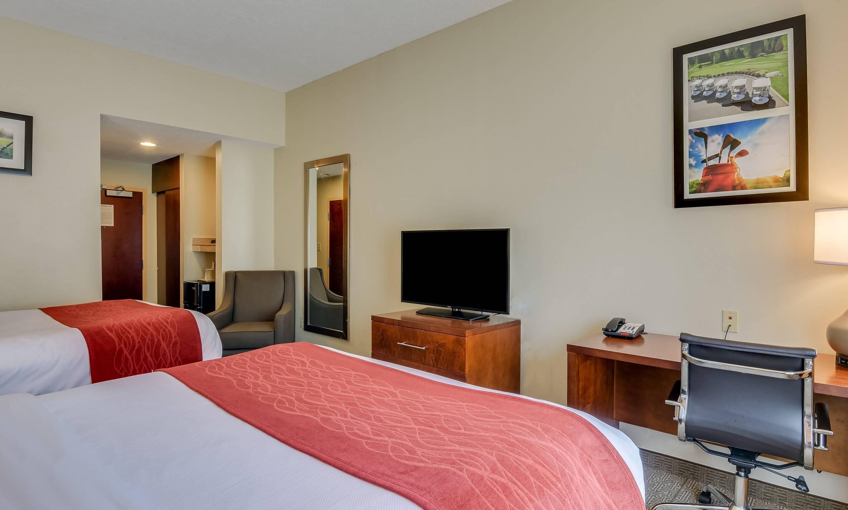 A hotel room with two beds, a TV, a desk with a phone, and a chair.
